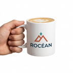 Mug en céramique blanc avec logo montagne et latte, tenu à la main sur fond blanc