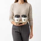 Femme portant quatre cafés sur un porte-gobelets en carton soutenu par une main, gobelets blancs et couvercles noirs sur fond blanc
